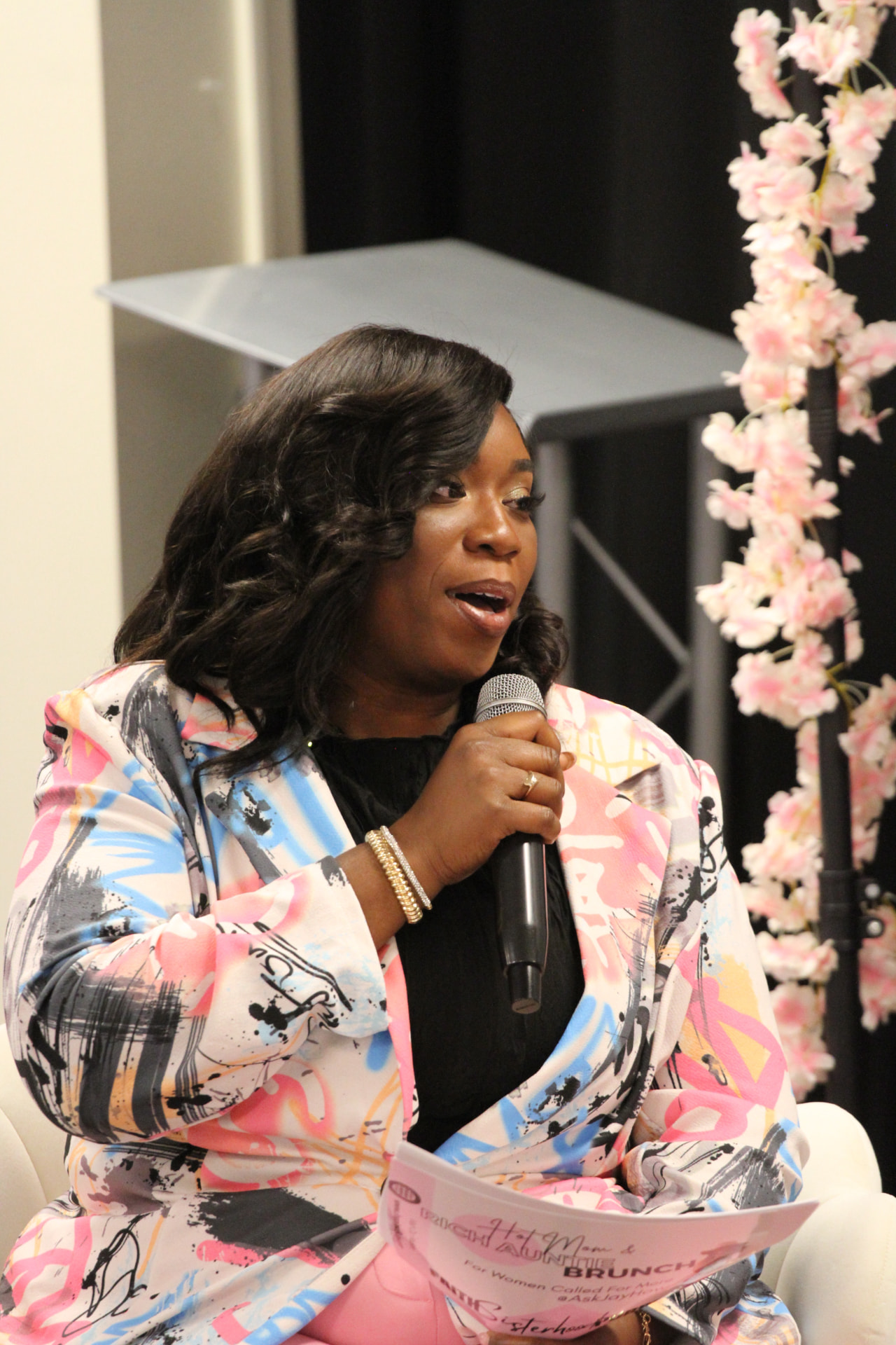 Jay How speaking into a microphone beside pink florals